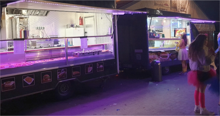 Vor dem Start in den Abend: Der große Foodtruck, bestehend aus zwei Wagen, steht stimmungsvoll beleuchtet neben einem Festzelt.
